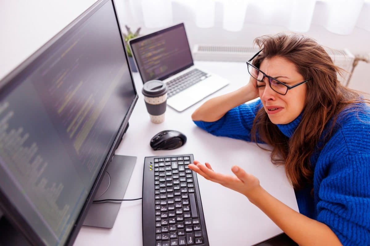 A frustrated designer with her head in her hand at a desk with two screens